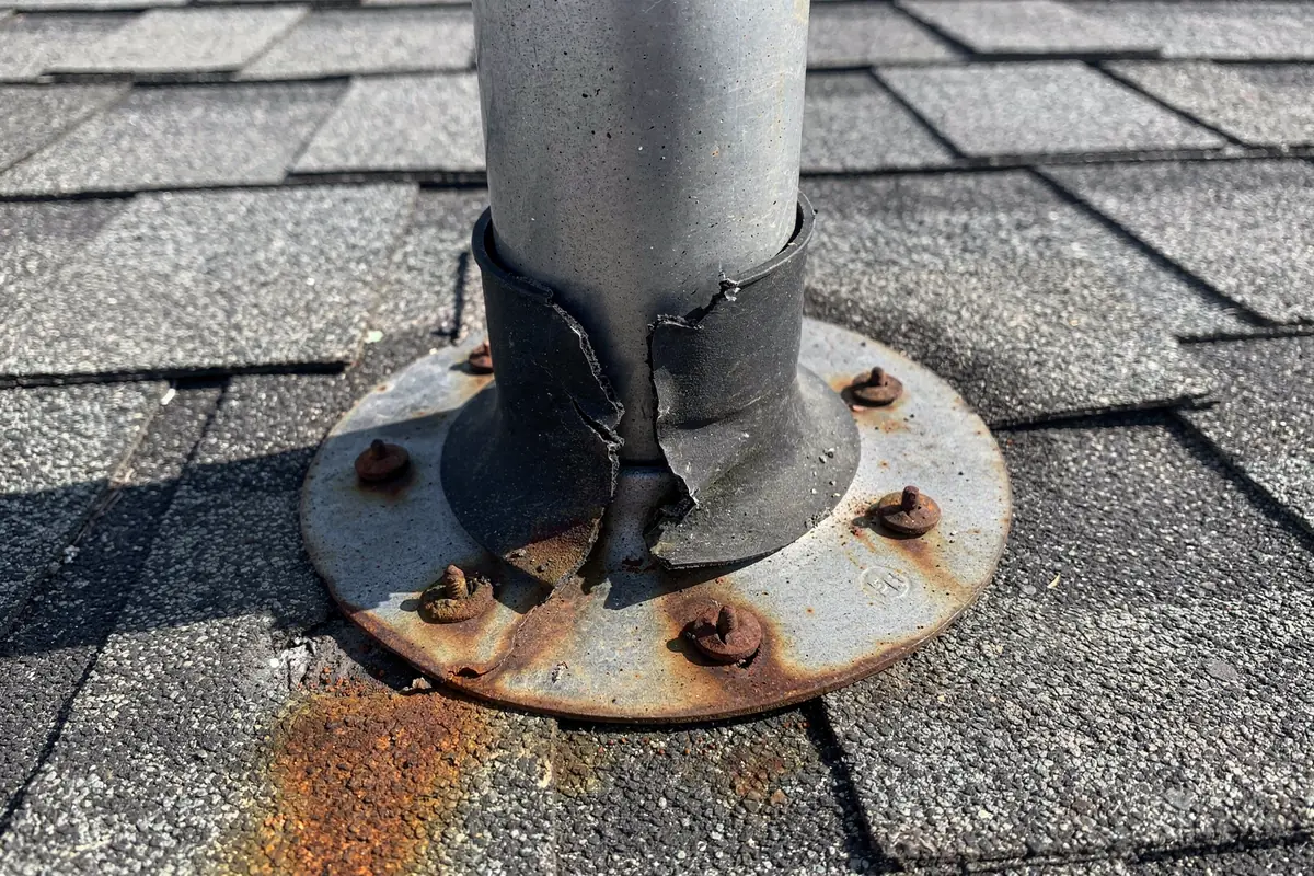 A plumbing vent flashing with a cracked rubber collar and corroded nail heads.